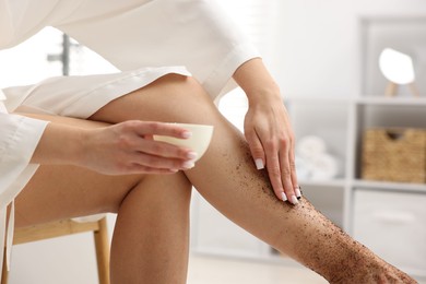 Photo of Woman applying body scrub onto her leg indoors, closeup
