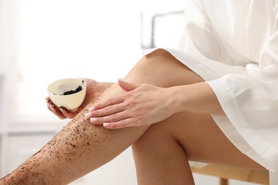 Photo of Woman applying body scrub onto her leg indoors, closeup