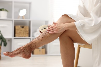 Photo of Woman applying body scrub onto her leg indoors, closeup