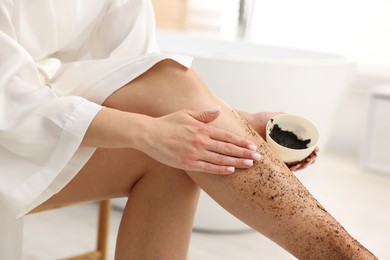 Photo of Woman applying body scrub onto her leg indoors, closeup
