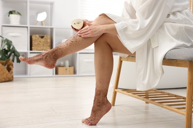 Photo of Woman applying body scrub onto her leg indoors, closeup