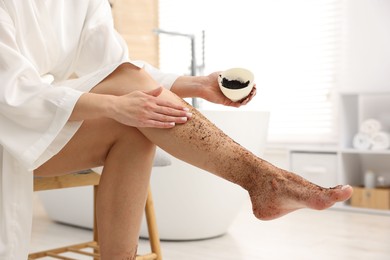 Photo of Woman applying body scrub onto her leg indoors, closeup
