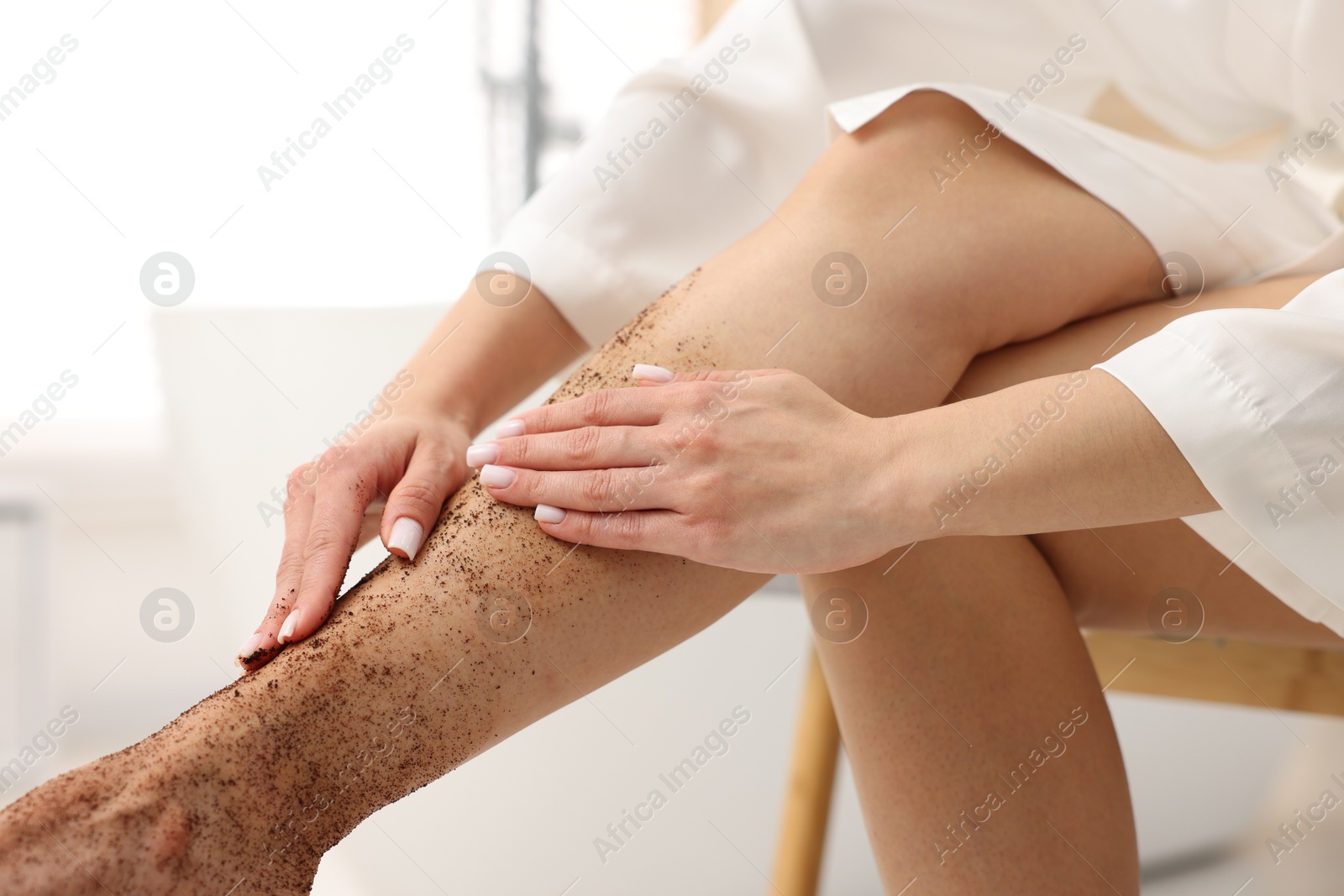 Woman applying body scrub onto her leg indoors, closeup Photo of Woman applying body scrub onto her leg indoors, closeup