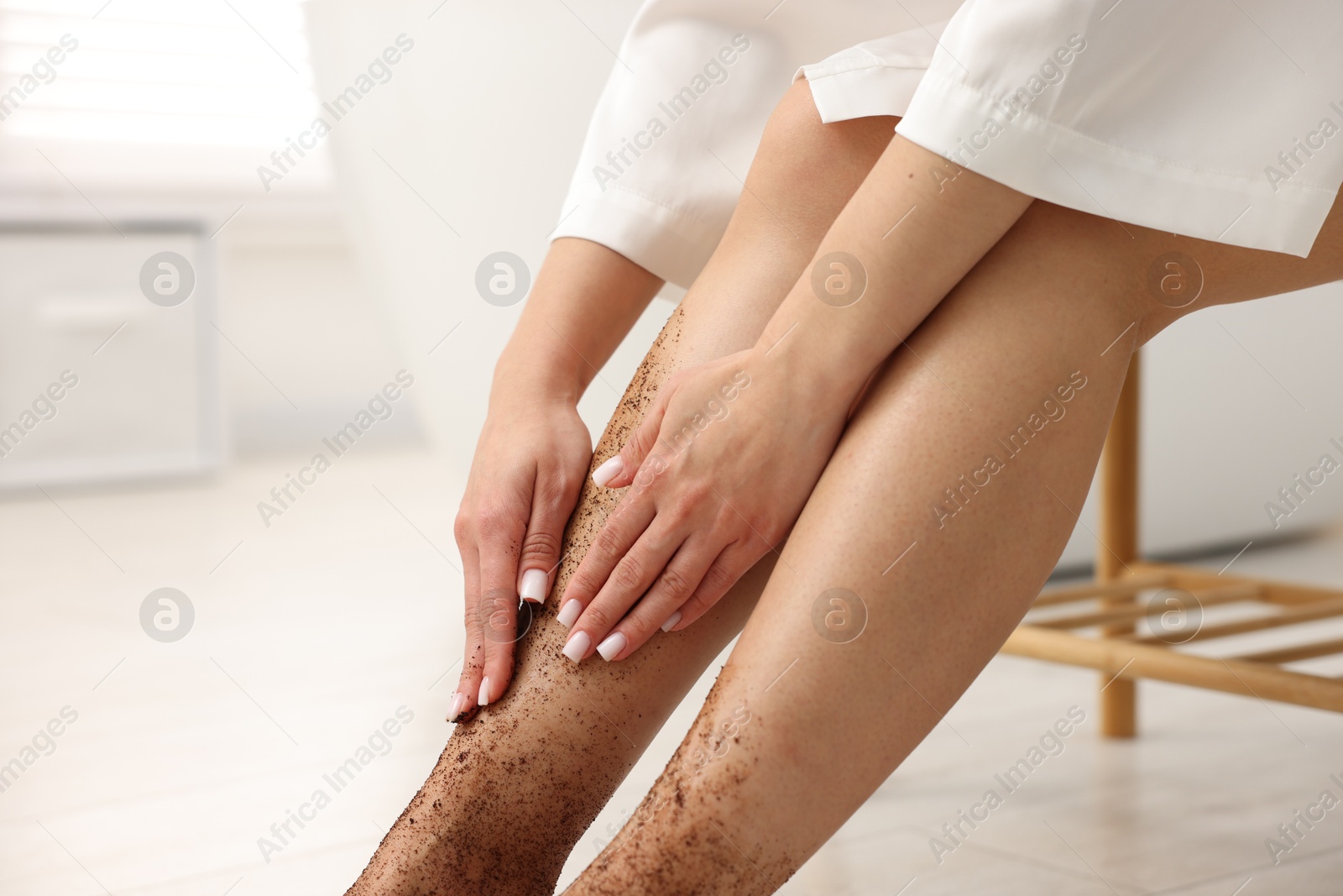 Woman applying body scrub onto her leg indoors, closeup Photo of Woman applying body scrub onto her leg indoors, closeup