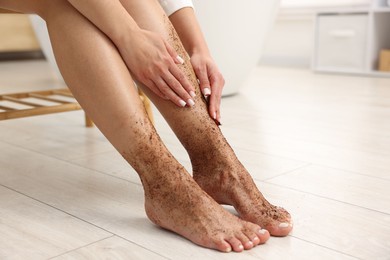 Photo of Woman applying body scrub onto her leg indoors, closeup