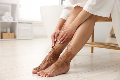 Photo of Woman applying body scrub onto her leg indoors, closeup. Space for text