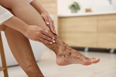 Photo of Woman applying body scrub onto her leg indoors, closeup