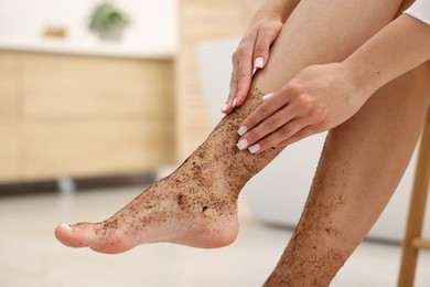 Photo of Woman applying body scrub onto her leg indoors, closeup