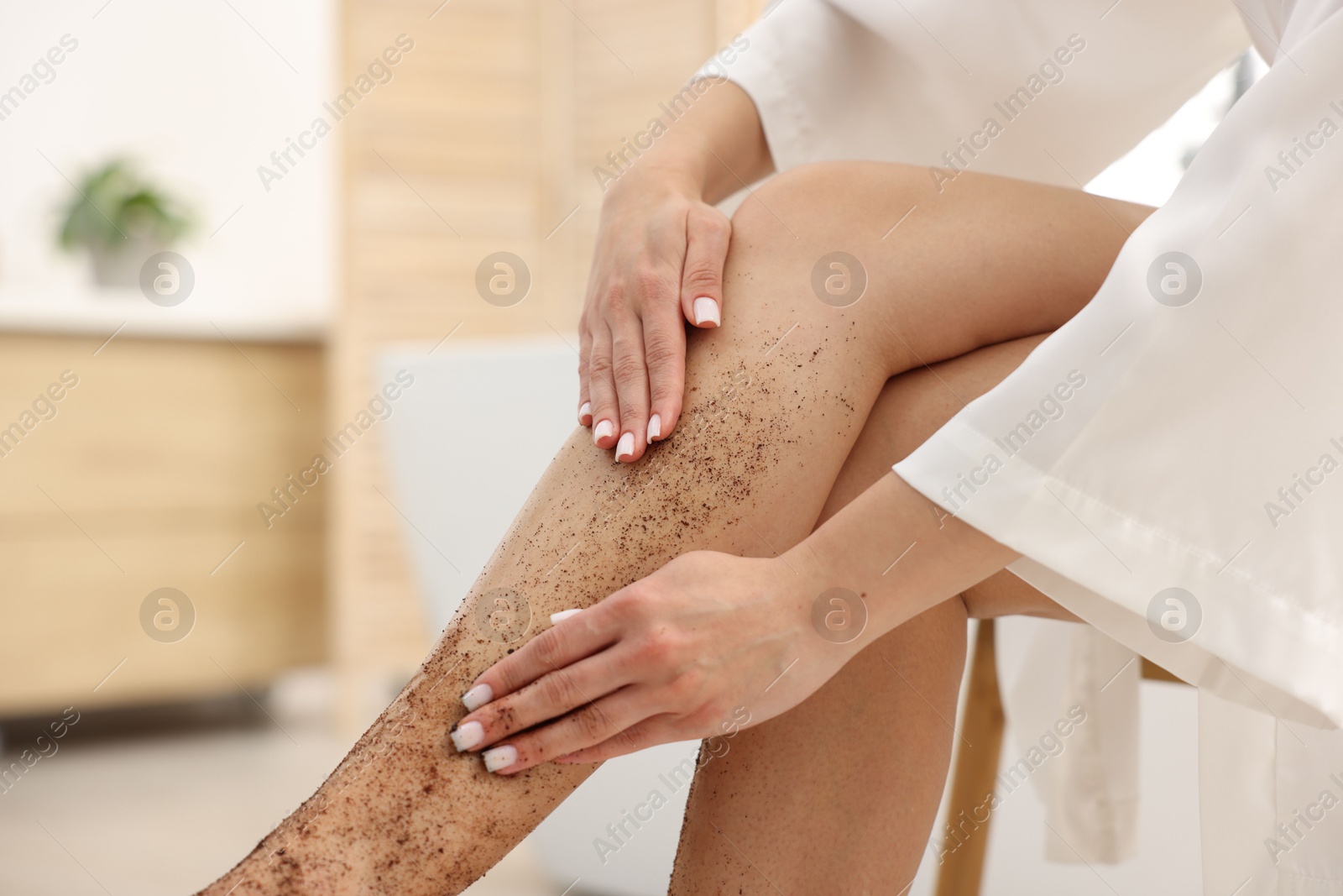 Woman applying body scrub onto her leg indoors, closeup Photo of Woman applying body scrub onto her leg indoors, closeup