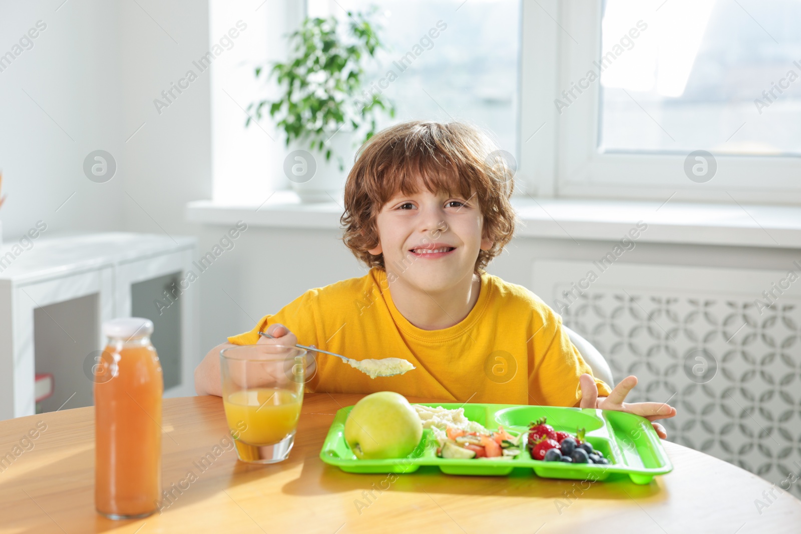 Cute little boy eating lunch at wooden table in school Photo of Cute little boy eating lunch at wooden table in school