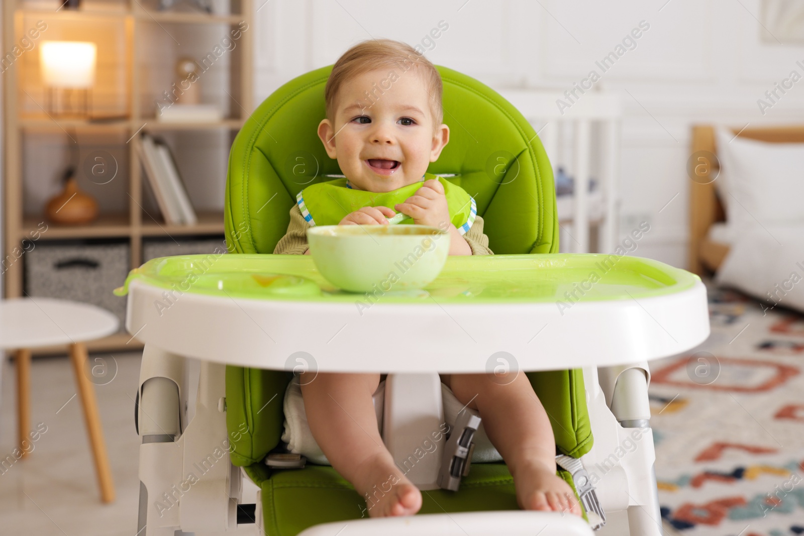 Cute little baby eating healthy food in high chair indoors Photo of Cute little baby eating healthy food in high chair indoors