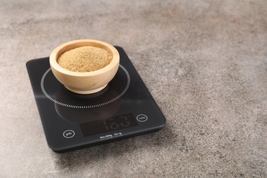 Digital kitchen scale with bowl of sugar on grey table, closeup. Space for text