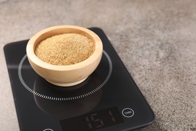 Photo of Digital kitchen scale with bowl of sugar on grey table, closeup