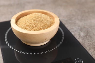 Photo of Digital kitchen scale with bowl of sugar on grey table, closeup