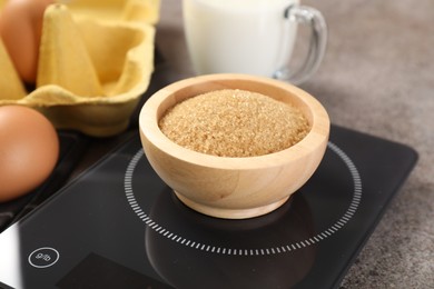 Photo of Digital kitchen scale with bowl of brown sugar and other products on grey table, closeup