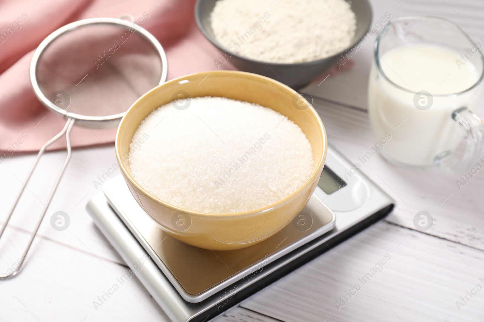 Digital kitchen scale with bowl of sugar and other products on white wooden table, closeup Photo of Digital kitchen scale with bowl of sugar and other products on white wooden table, closeup