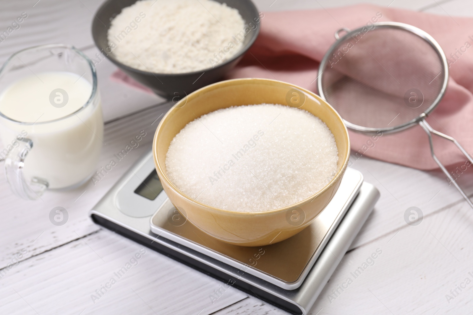 Digital kitchen scale with bowl of sugar and other products on white wooden table, closeup Photo of Digital kitchen scale with bowl of sugar and other products on white wooden table, closeup