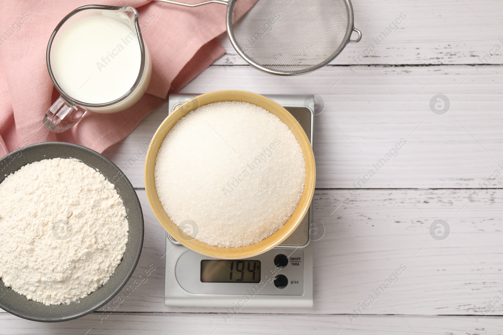 Digital kitchen scale with bowl of sugar and other products on white wooden table, flat lay. Space for text Photo of Digital kitchen scale with bowl of sugar and other products on white wooden table, flat lay. Space for text