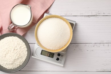 Photo of Digital kitchen scale with bowl of sugar and other products on white wooden table, flat lay. Space for text