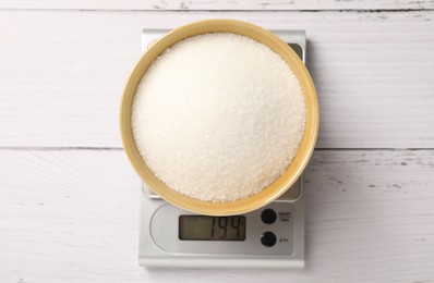 Photo of Digital kitchen scale with bowl of sugar on wooden table, top view