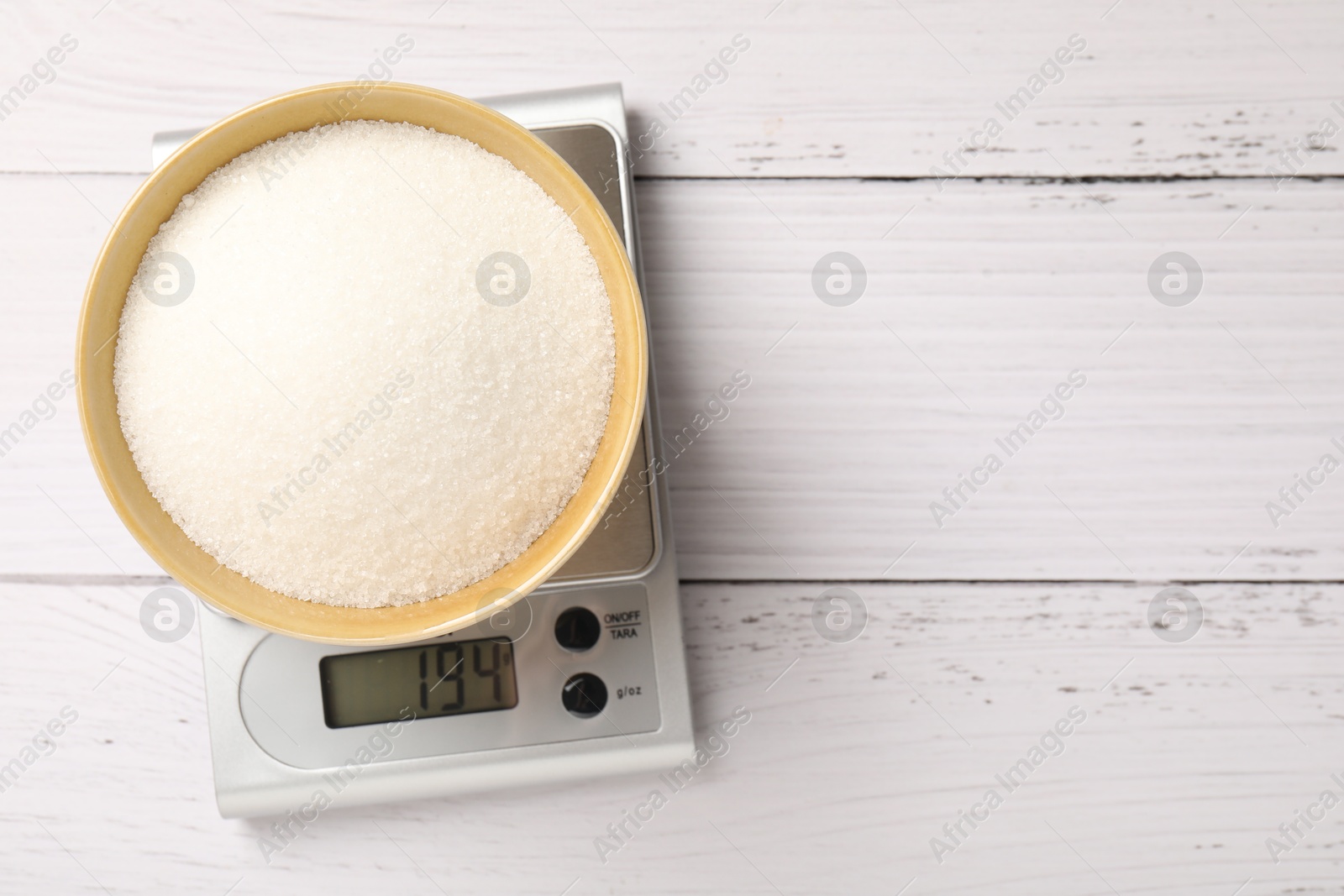 Digital kitchen scale with bowl of sugar on wooden table, top view. Space for text Photo of Digital kitchen scale with bowl of sugar on wooden table, top view. Space for text