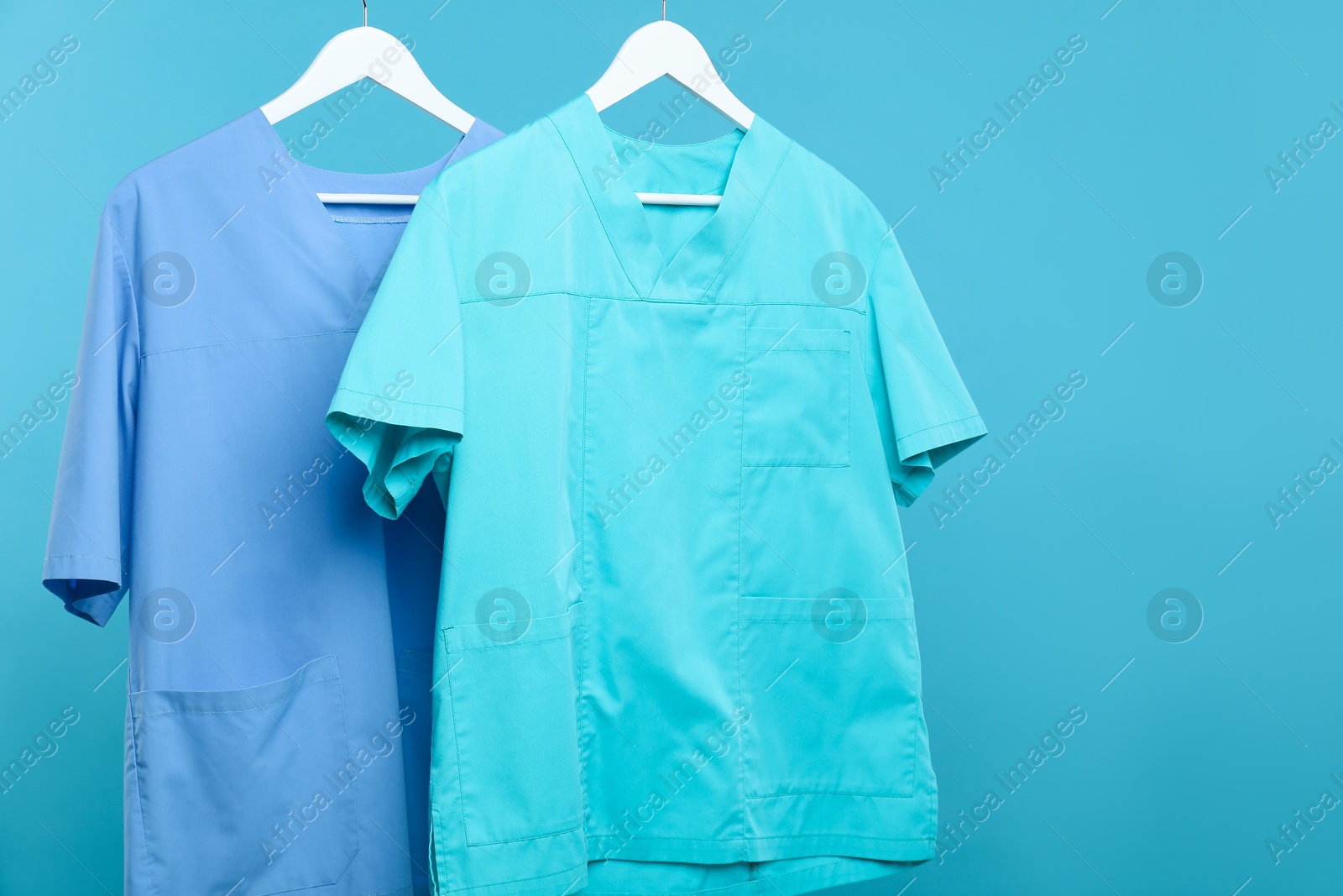 Medical workers uniforms on hangers against blue background Photo of Medical workers uniforms on hangers against blue background