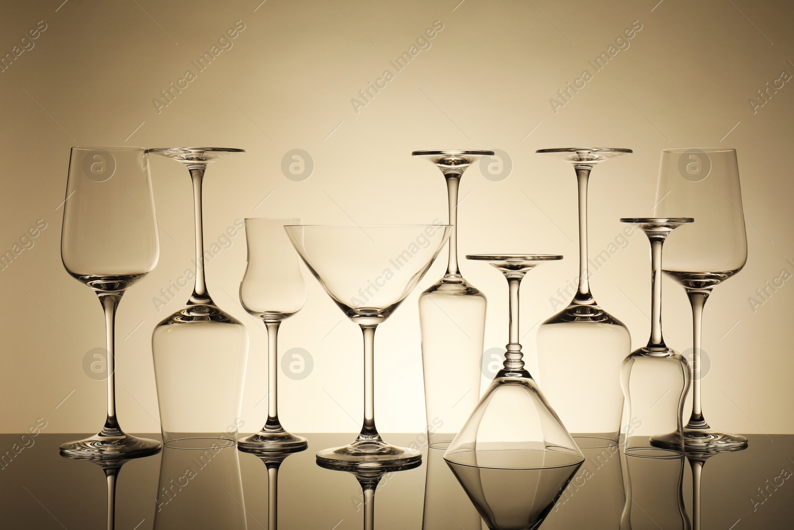 Many empty clean glasses on mirror surface against beige background Photo of Many empty clean glasses on mirror surface against beige background