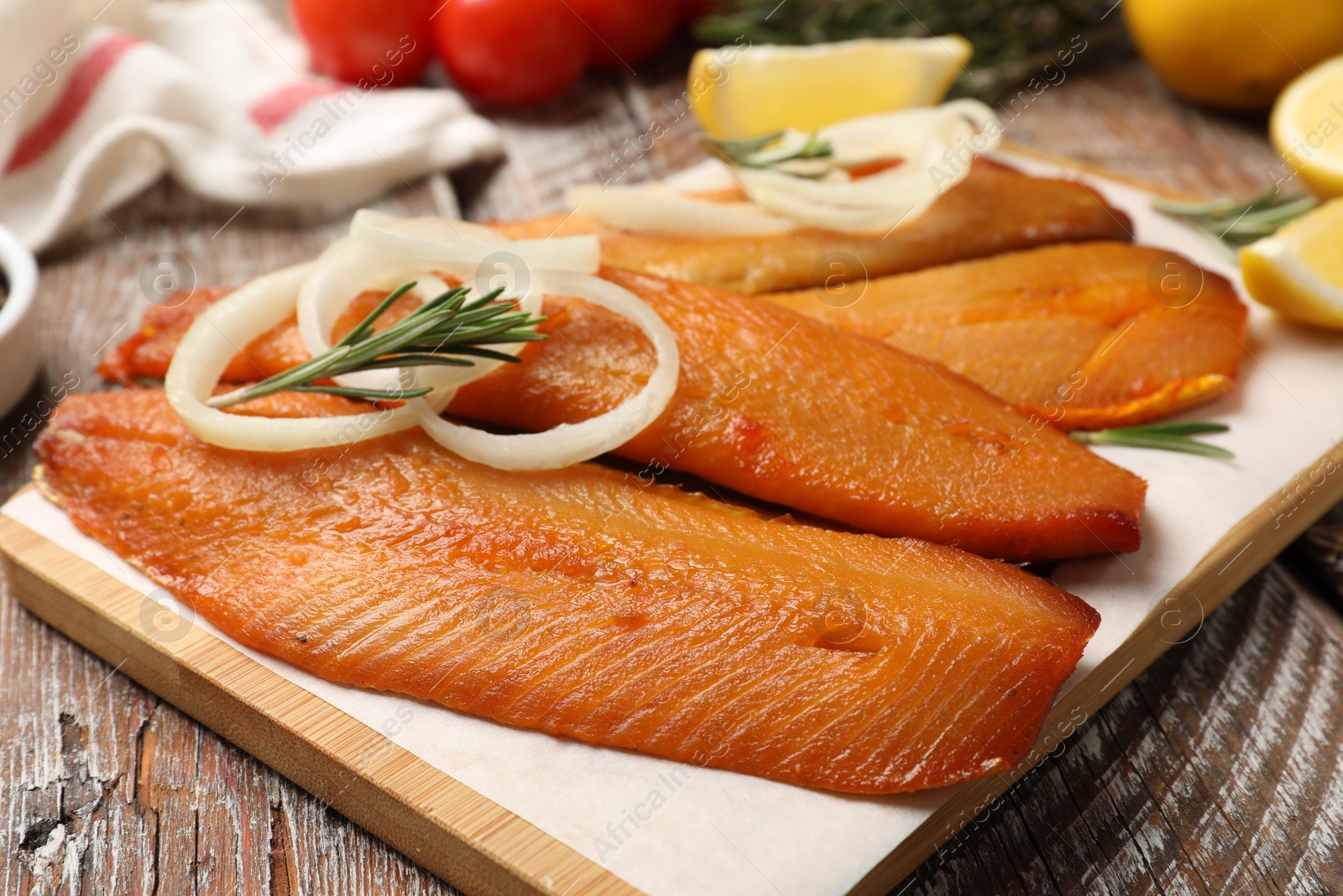 Photo of Delicious smoked herring fillets with lemon slices, onions and rosemary on wooden table, closeup