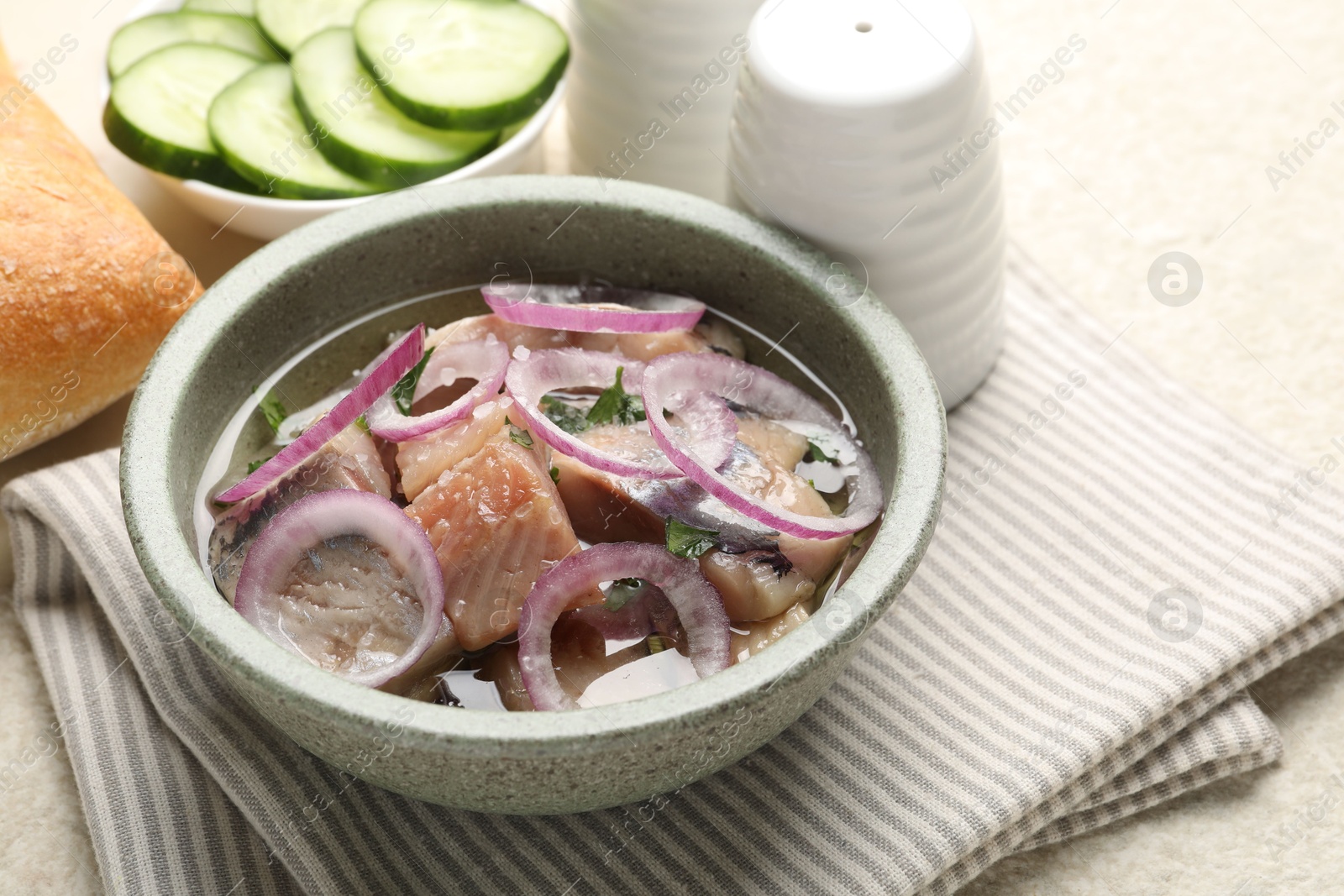 Pieces of delicious herring with onions, cucumber slices and bread on light table, closeup Photo of Pieces of delicious herring with onions, cucumber slices and bread on light table, closeup