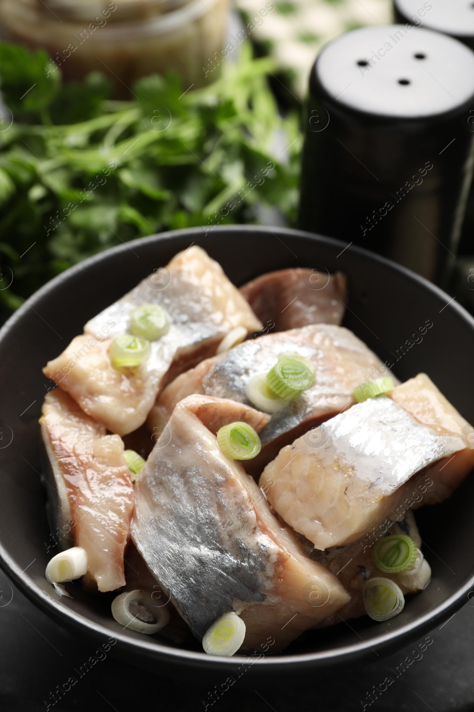 Pieces of delicious herring with green onions on black table, closeup Photo of Pieces of delicious herring with green onions on black table, closeup