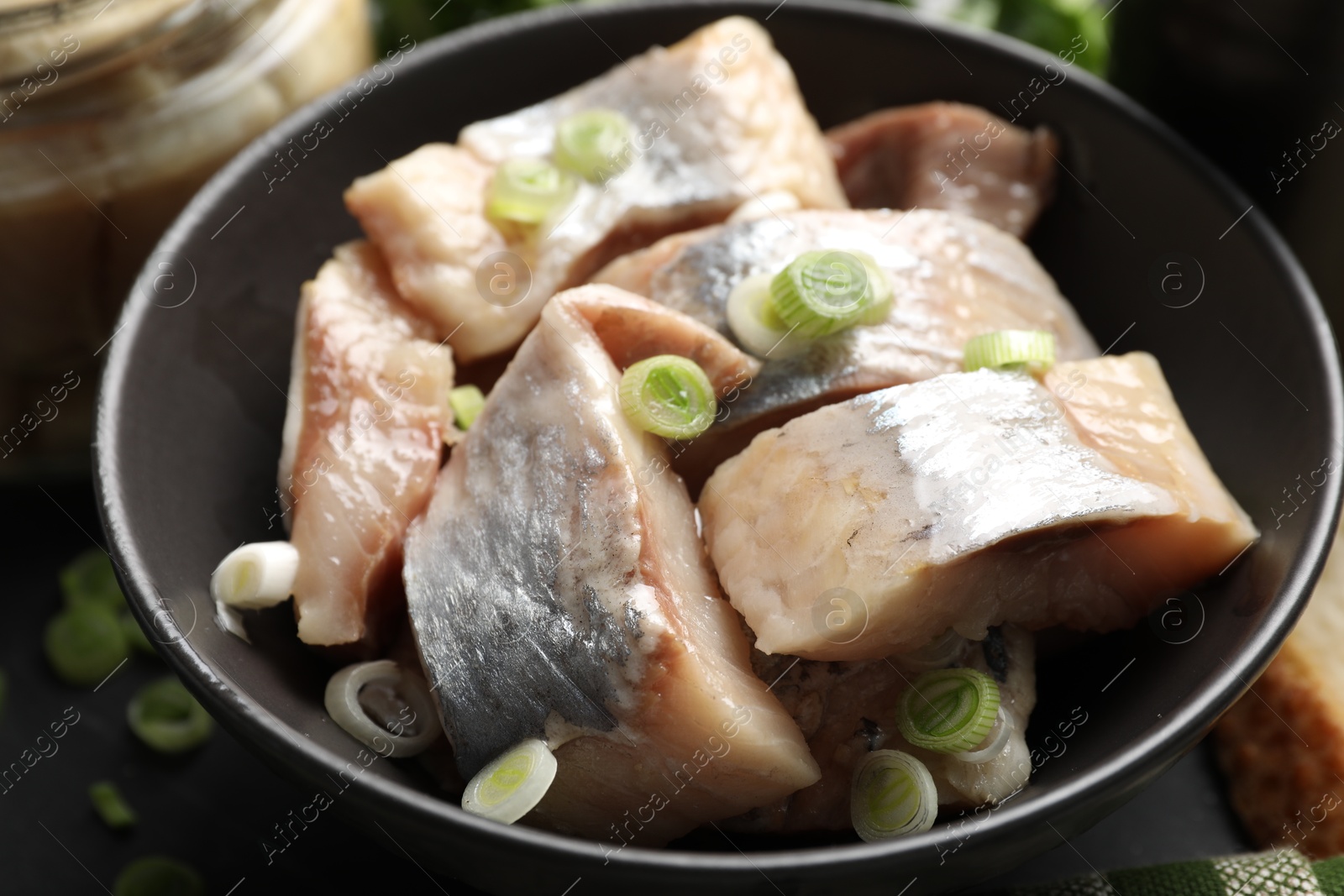 Pieces of delicious herring with green onions on black table, closeup Photo of Pieces of delicious herring with green onions on black table, closeup