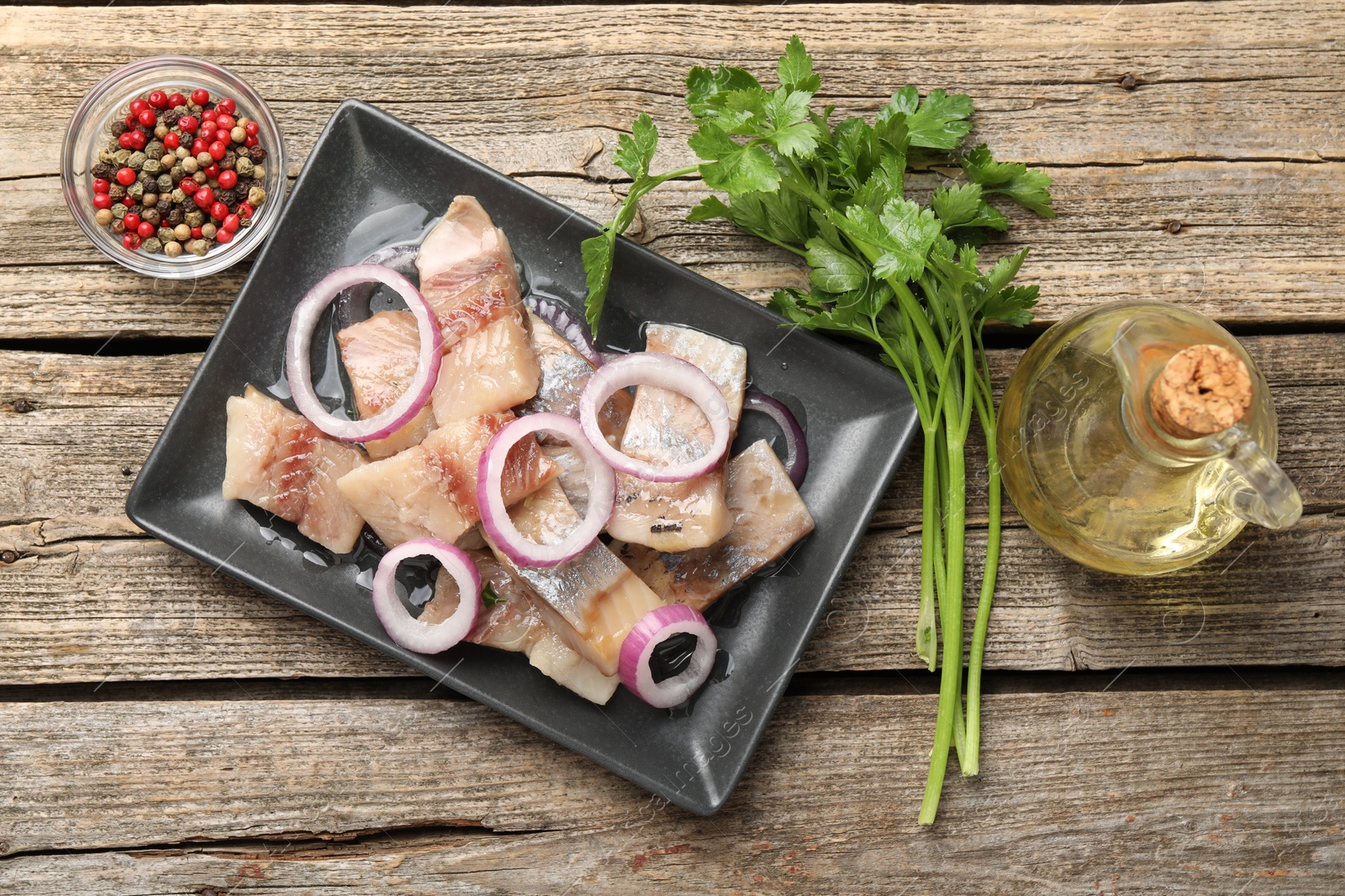 Pieces of herring with onions, peppercorns, oil and parsley on wooden table, flat lay Photo of Pieces of herring with onions, peppercorns, oil and parsley on wooden table, flat lay