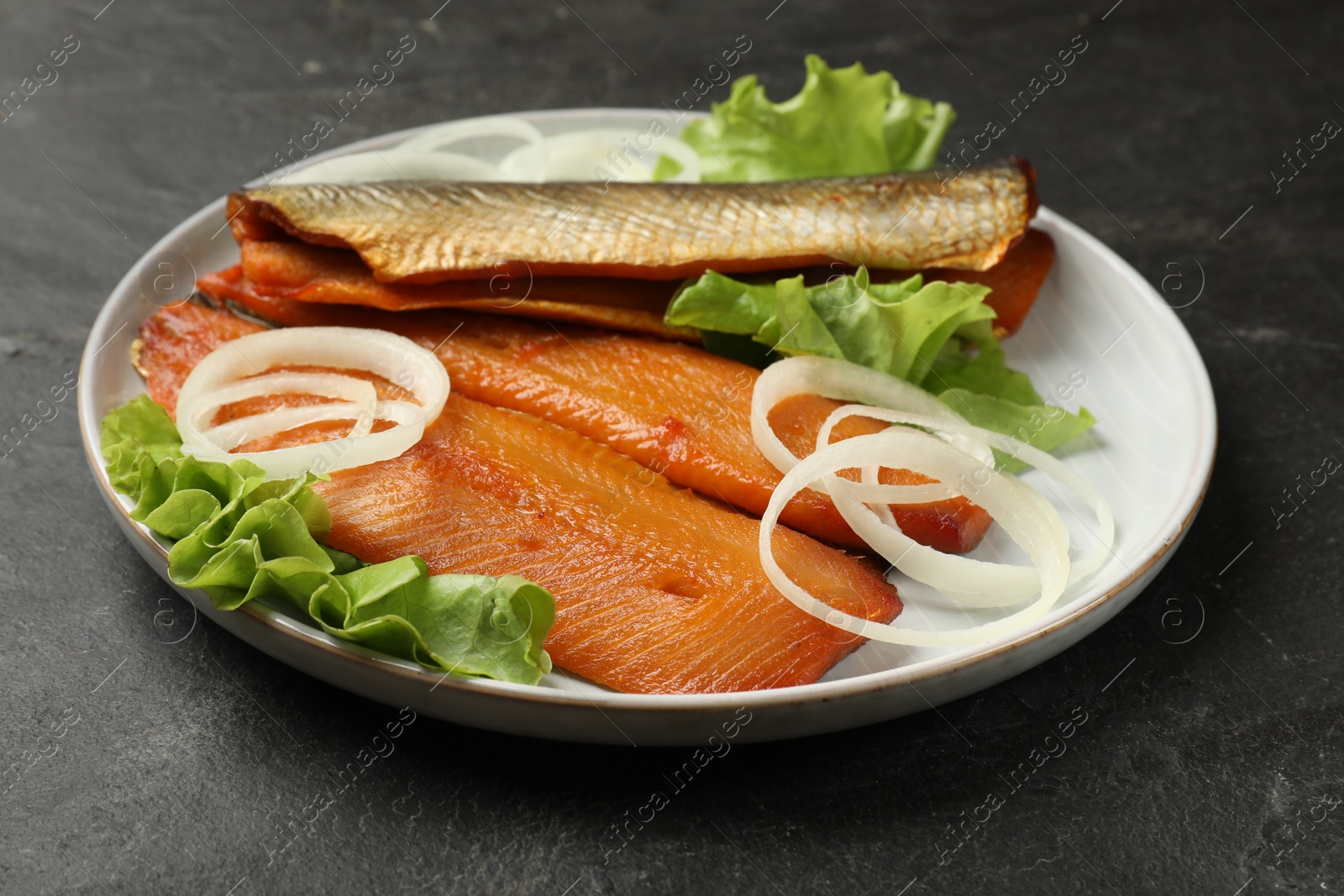 Delicious smoked herring fillets with onions and lettuce on black table, closeup Photo of Delicious smoked herring fillets with onions and lettuce on black table, closeup