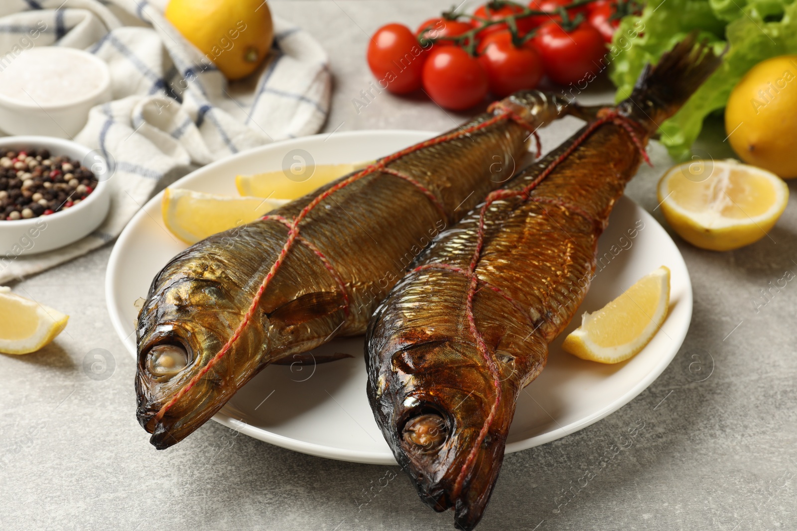 Delicious smoked herrings with lemon slices and other products on grey table, closeup Photo of Delicious smoked herrings with lemon slices and other products on grey table, closeup