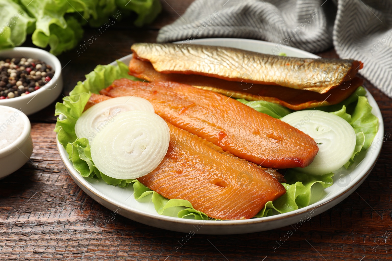 Delicious smoked herring fillets with onions and lettuce on wooden table, closeup Photo of Delicious smoked herring fillets with onions and lettuce on wooden table, closeup