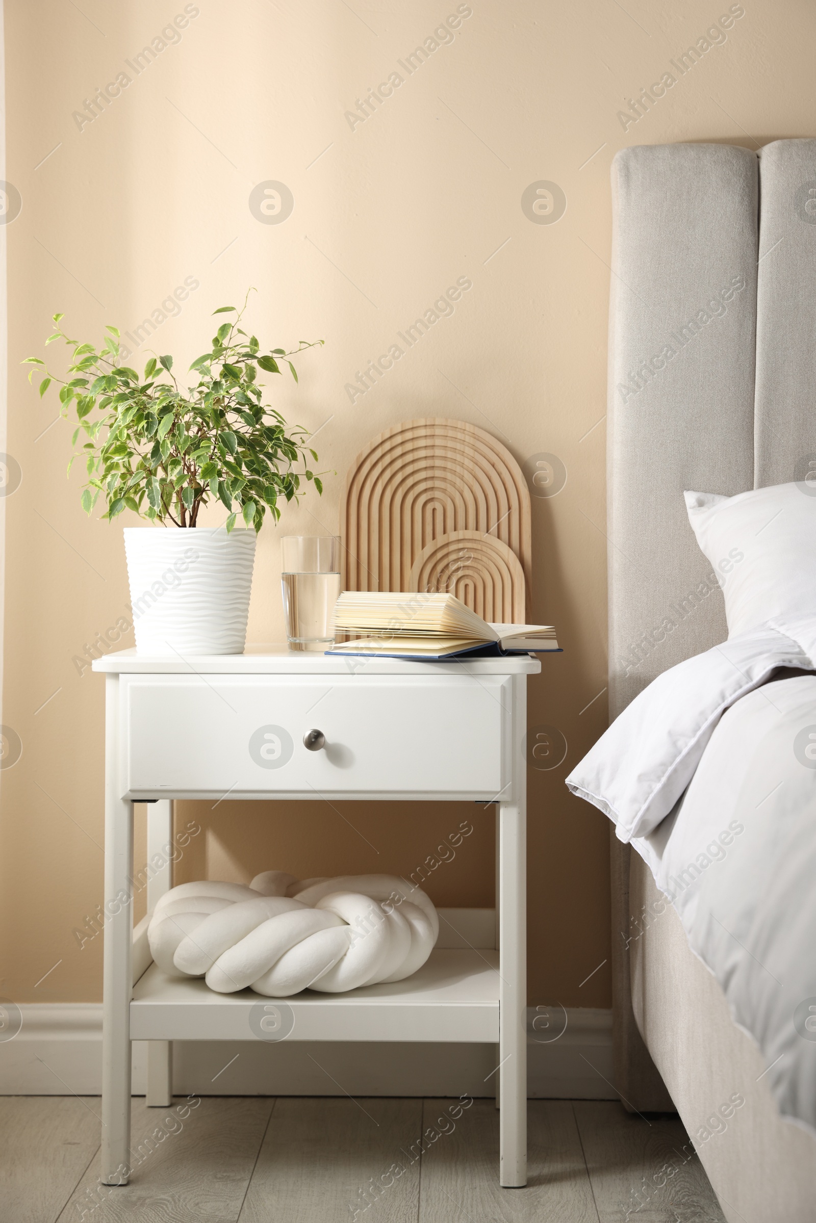 Bedside table with book, decor and glass of water near bed in room Photo of Bedside table with book, decor and glass of water near bed in room