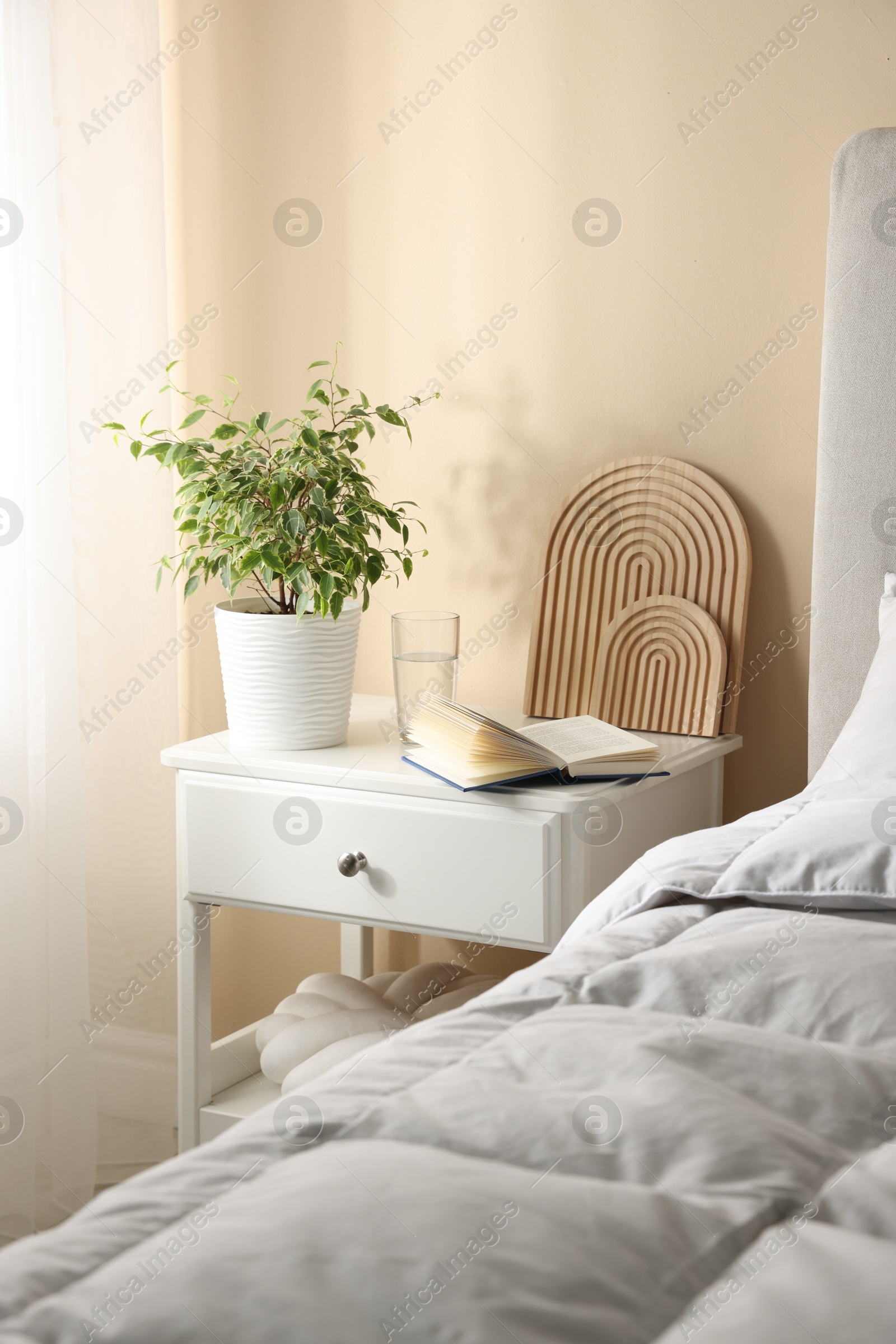 Bedside table with book, decor and glass of water near bed in room Photo of Bedside table with book, decor and glass of water near bed in room