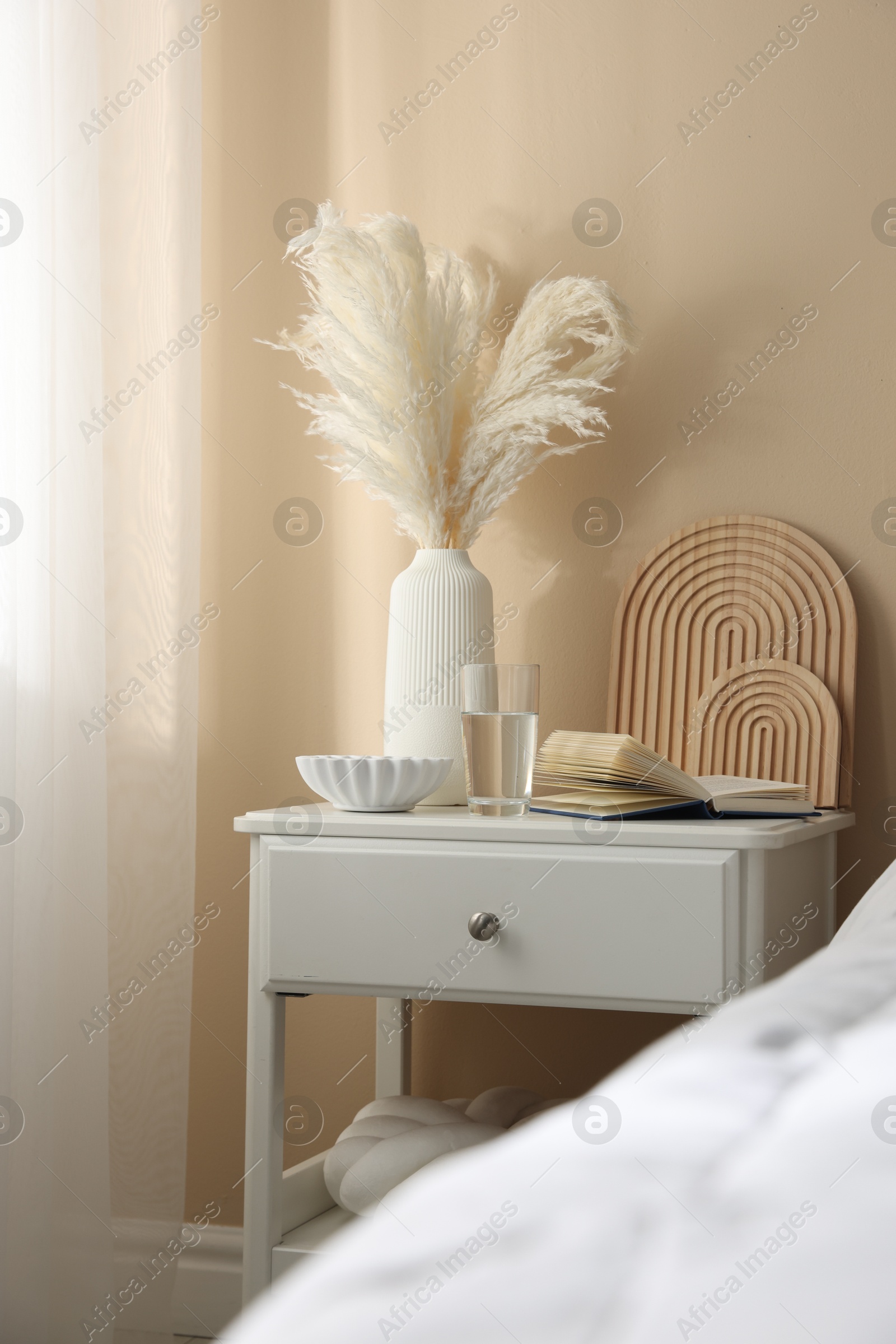 Bedside table with book, decor and glass of water near bed in room Photo of Bedside table with book, decor and glass of water near bed in room