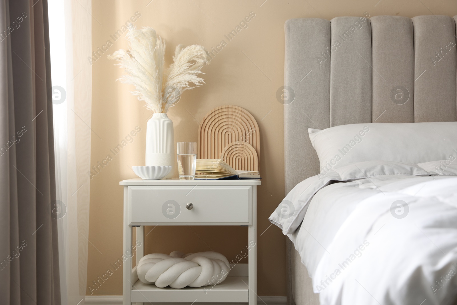 Bedside table with book, decor and glass of water near bed in room Photo of Bedside table with book, decor and glass of water near bed in room