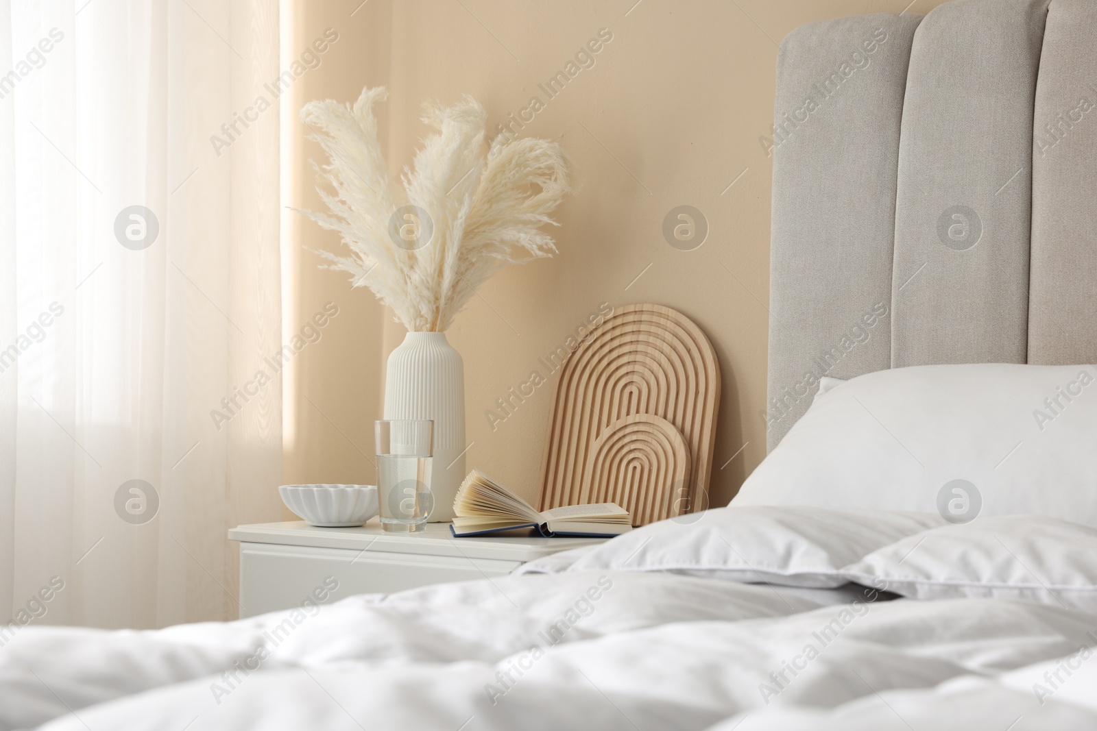 Bedside table with book, decor and glass of water near bed in room Photo of Bedside table with book, decor and glass of water near bed in room