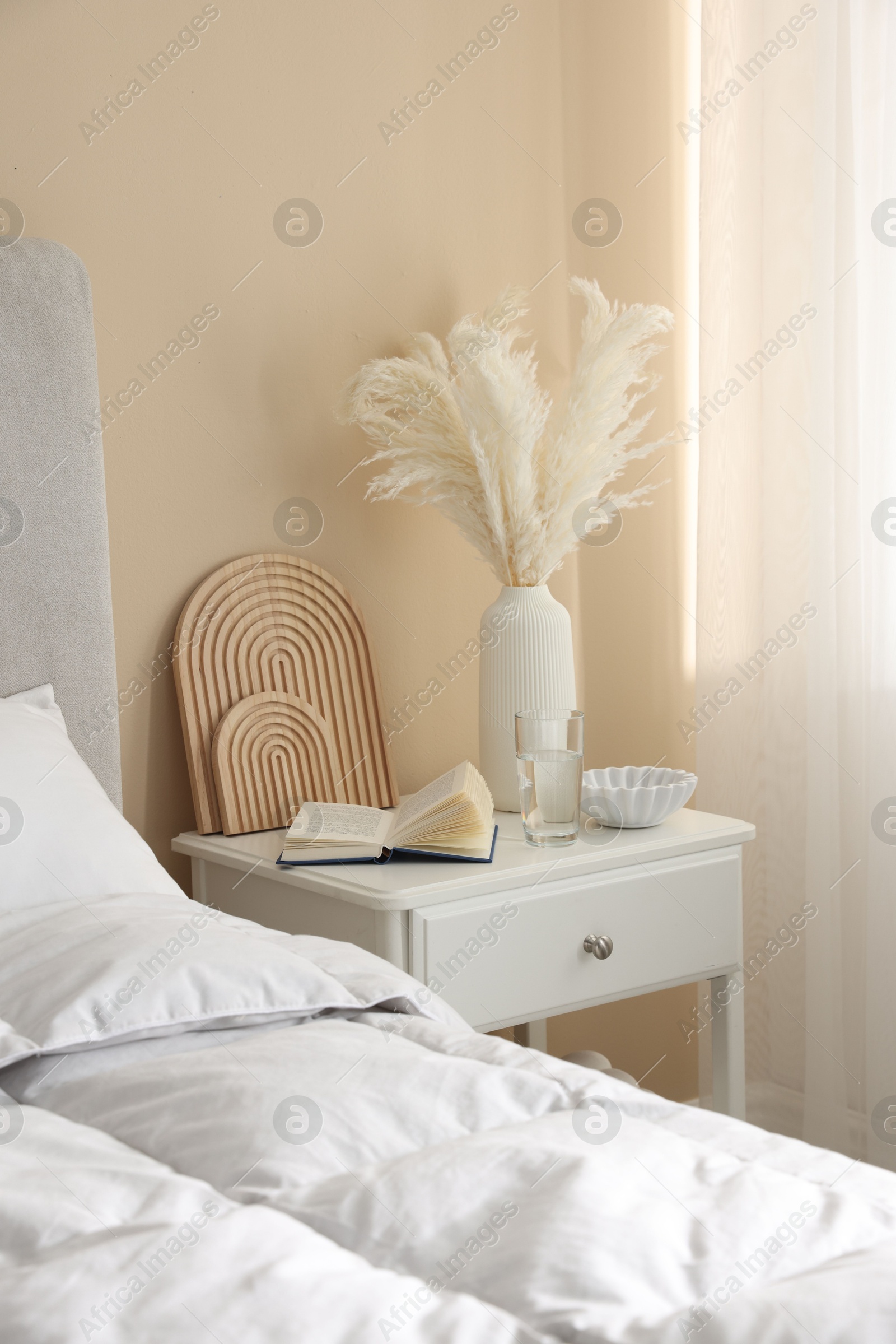 Bedside table with book, decor and glass of water near bed in room Photo of Bedside table with book, decor and glass of water near bed in room