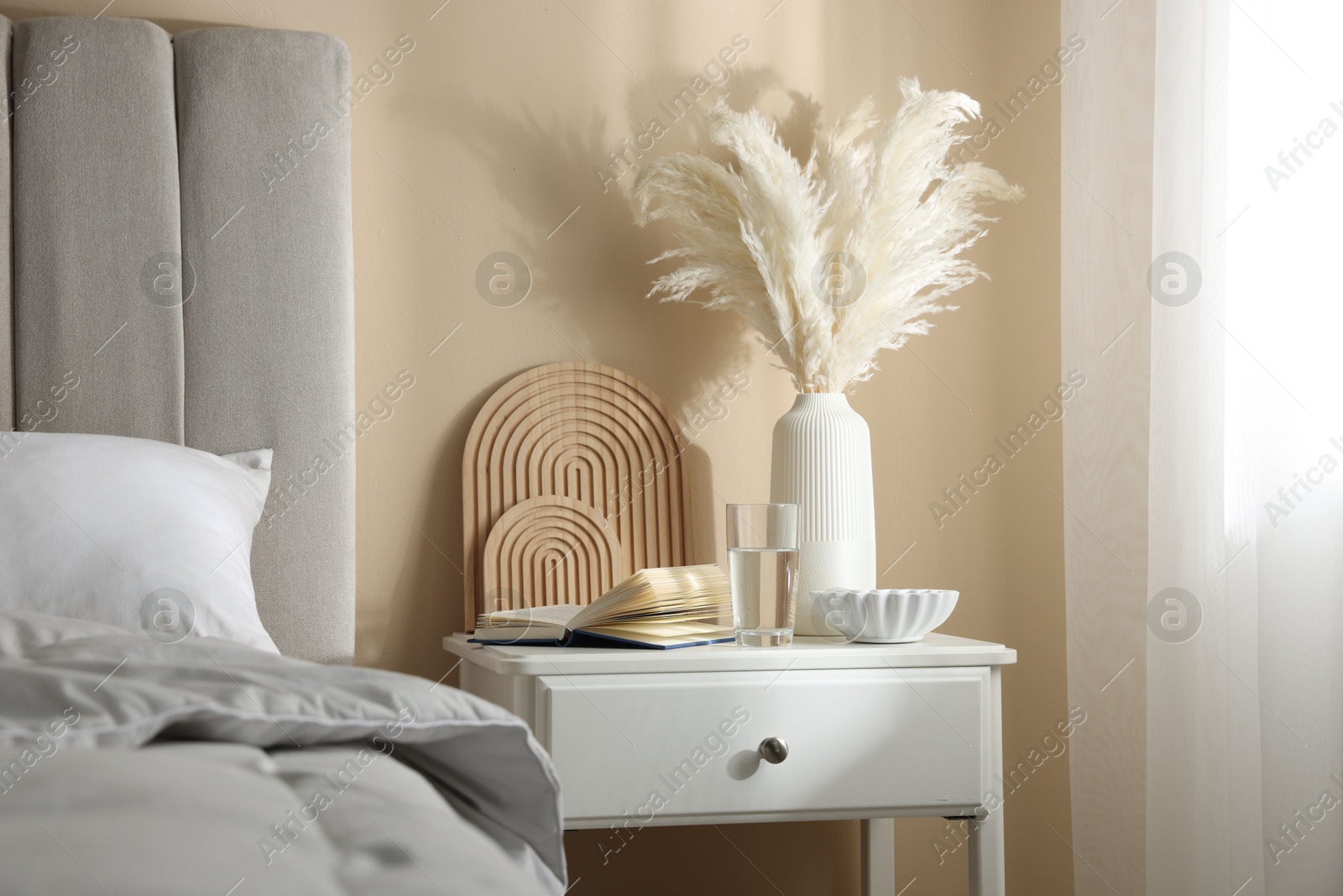Bedside table with book, decor and glass of water near bed in room Photo of Bedside table with book, decor and glass of water near bed in room
