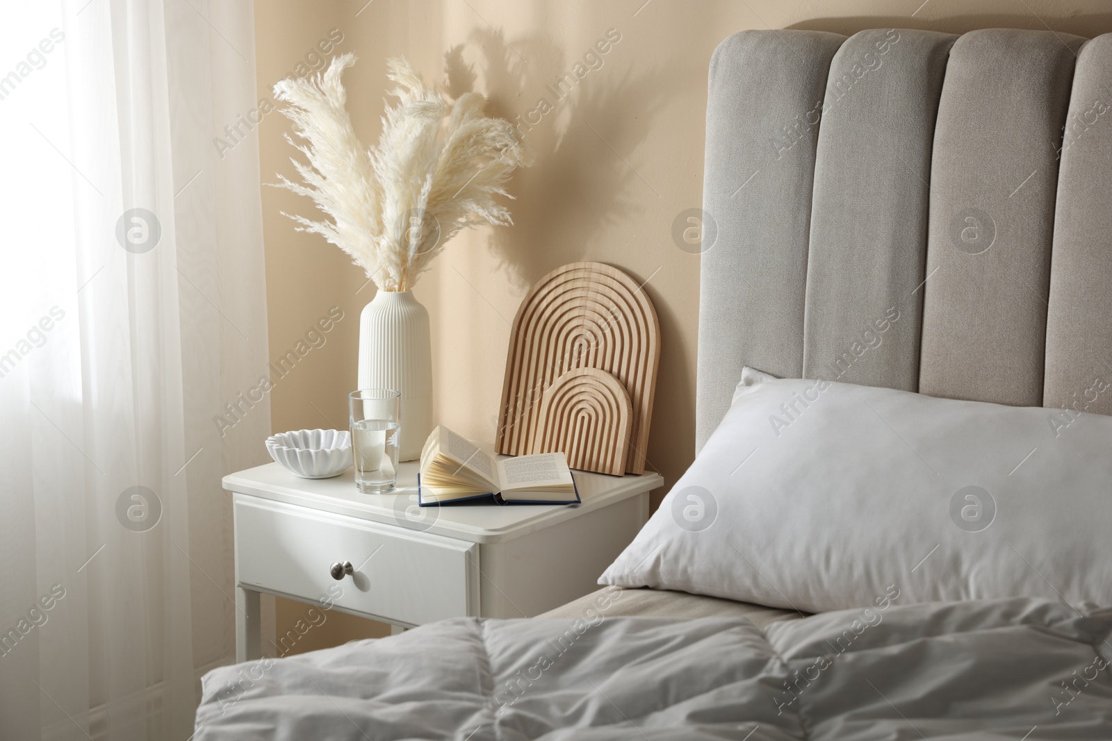 Bedside table with book, decor and glass of water near bed in room Photo of Bedside table with book, decor and glass of water near bed in room