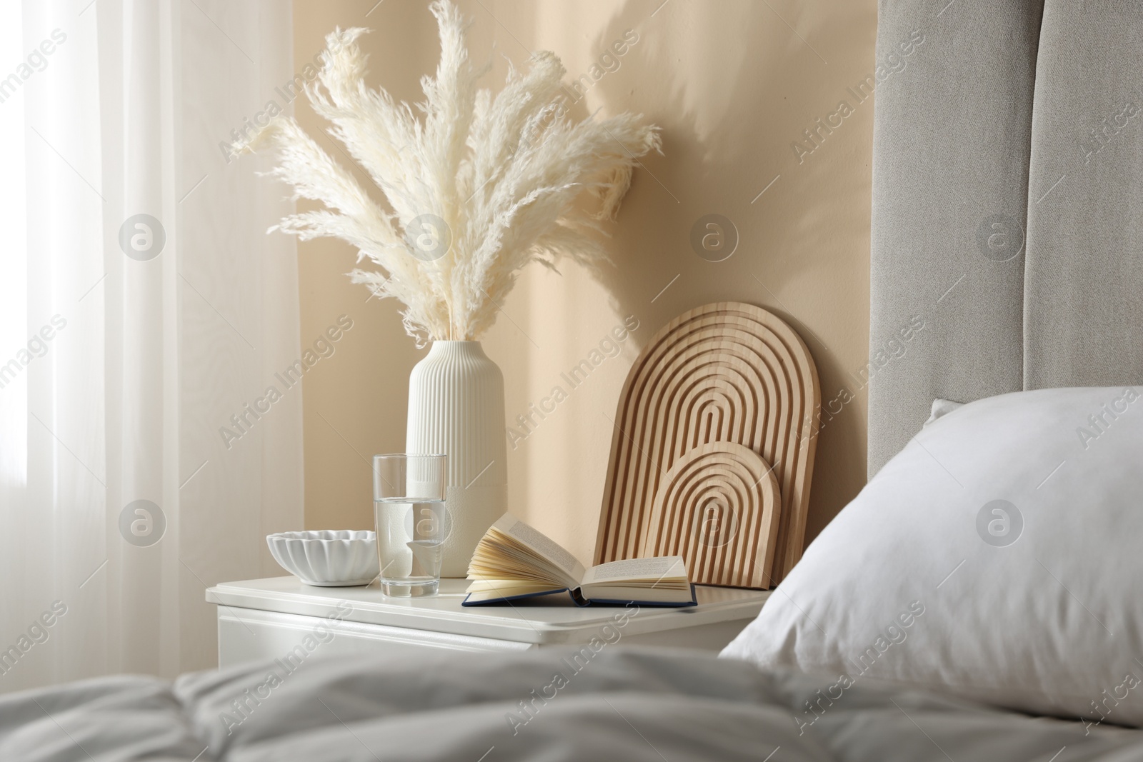 Bedside table with book, decor and glass of water near bed in room Photo of Bedside table with book, decor and glass of water near bed in room