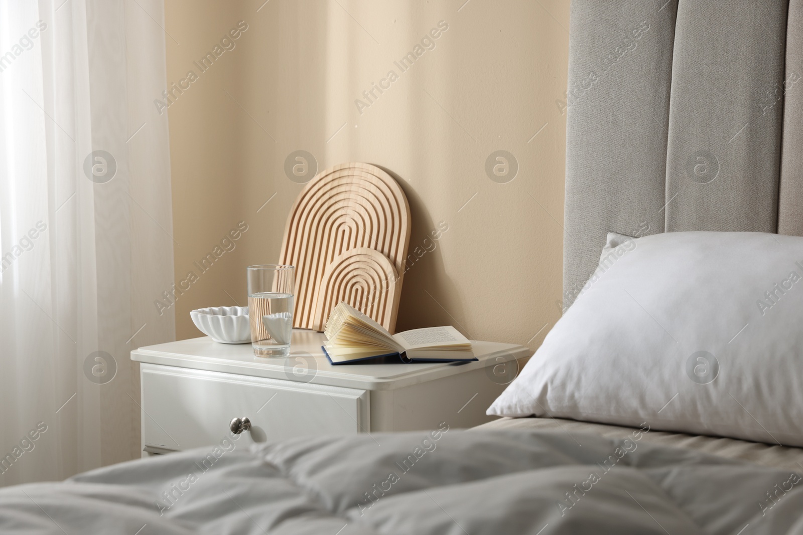 Bedside table with book, decor and glass of water near bed in room Photo of Bedside table with book, decor and glass of water near bed in room