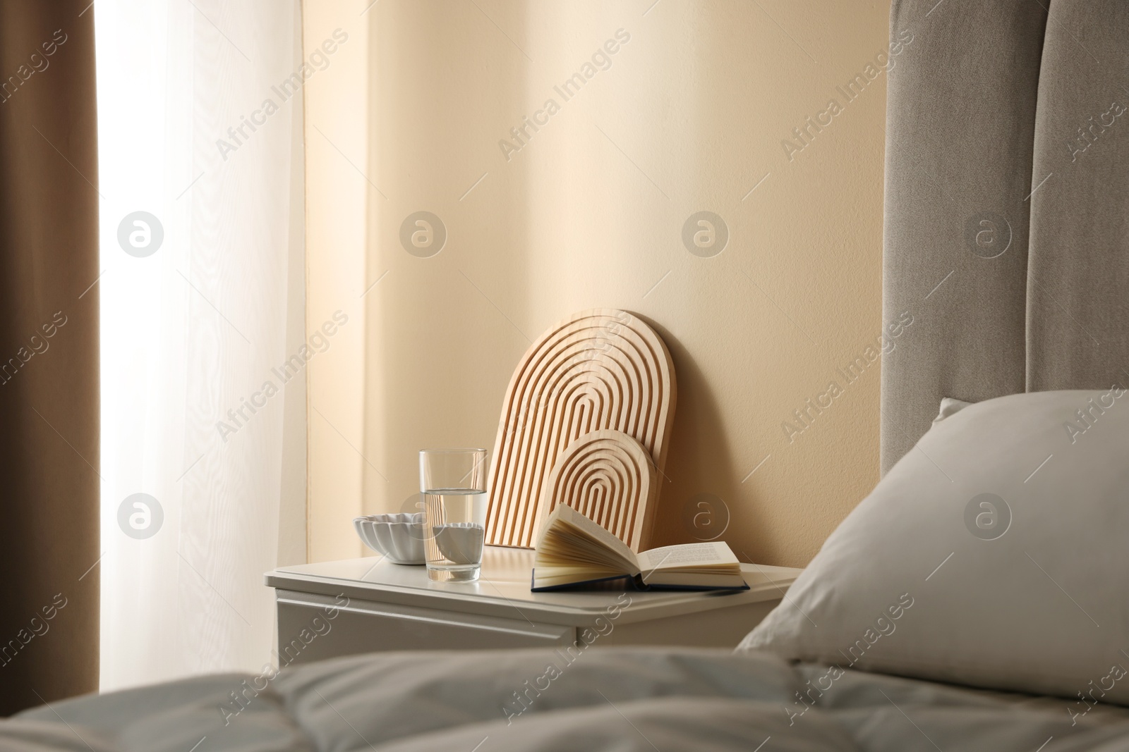 Bedside table with book, decor and glass of water near bed in room Photo of Bedside table with book, decor and glass of water near bed in room