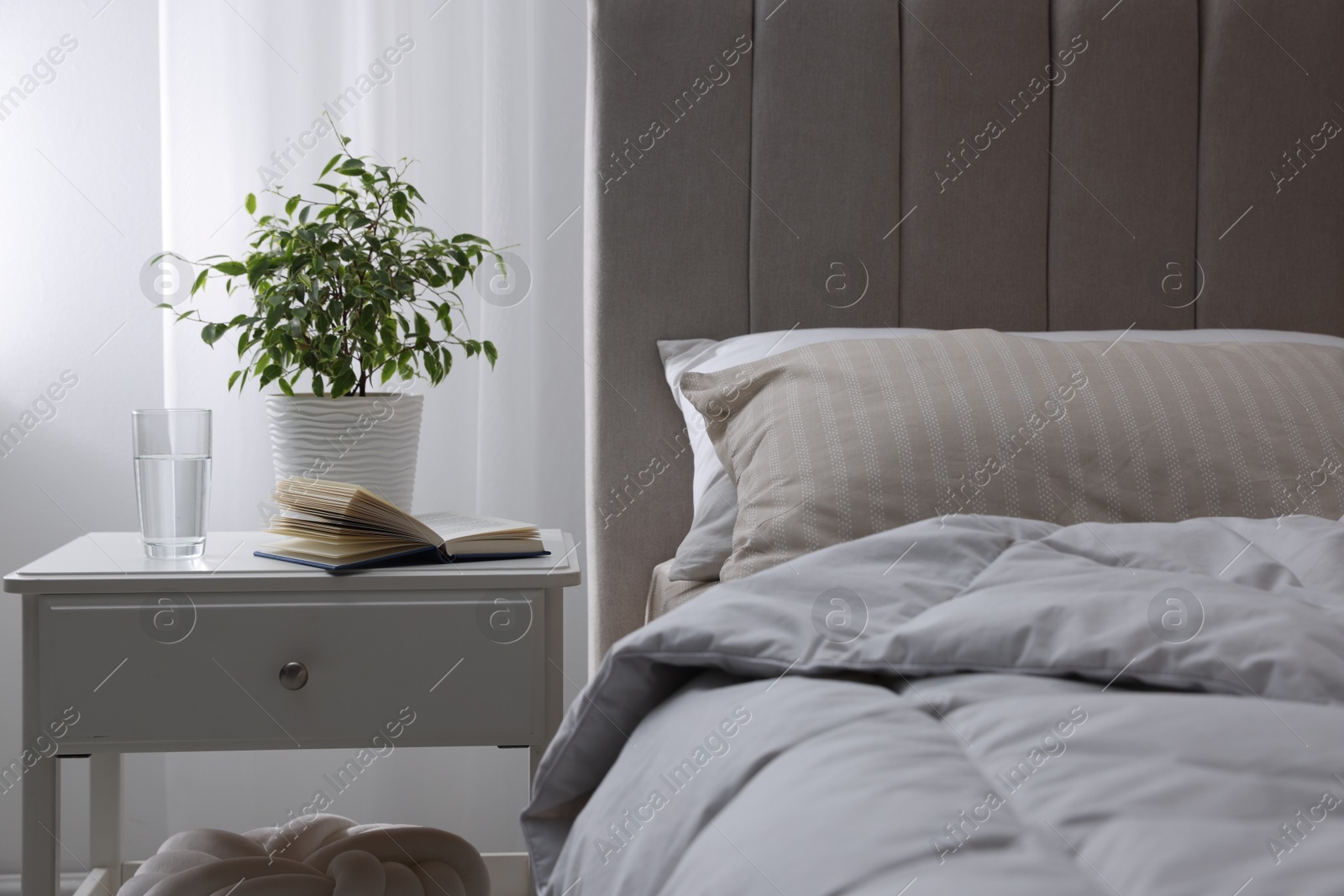Bedside table with book, houseplant and glass of water near bed in room Photo of Bedside table with book, houseplant and glass of water near bed in room