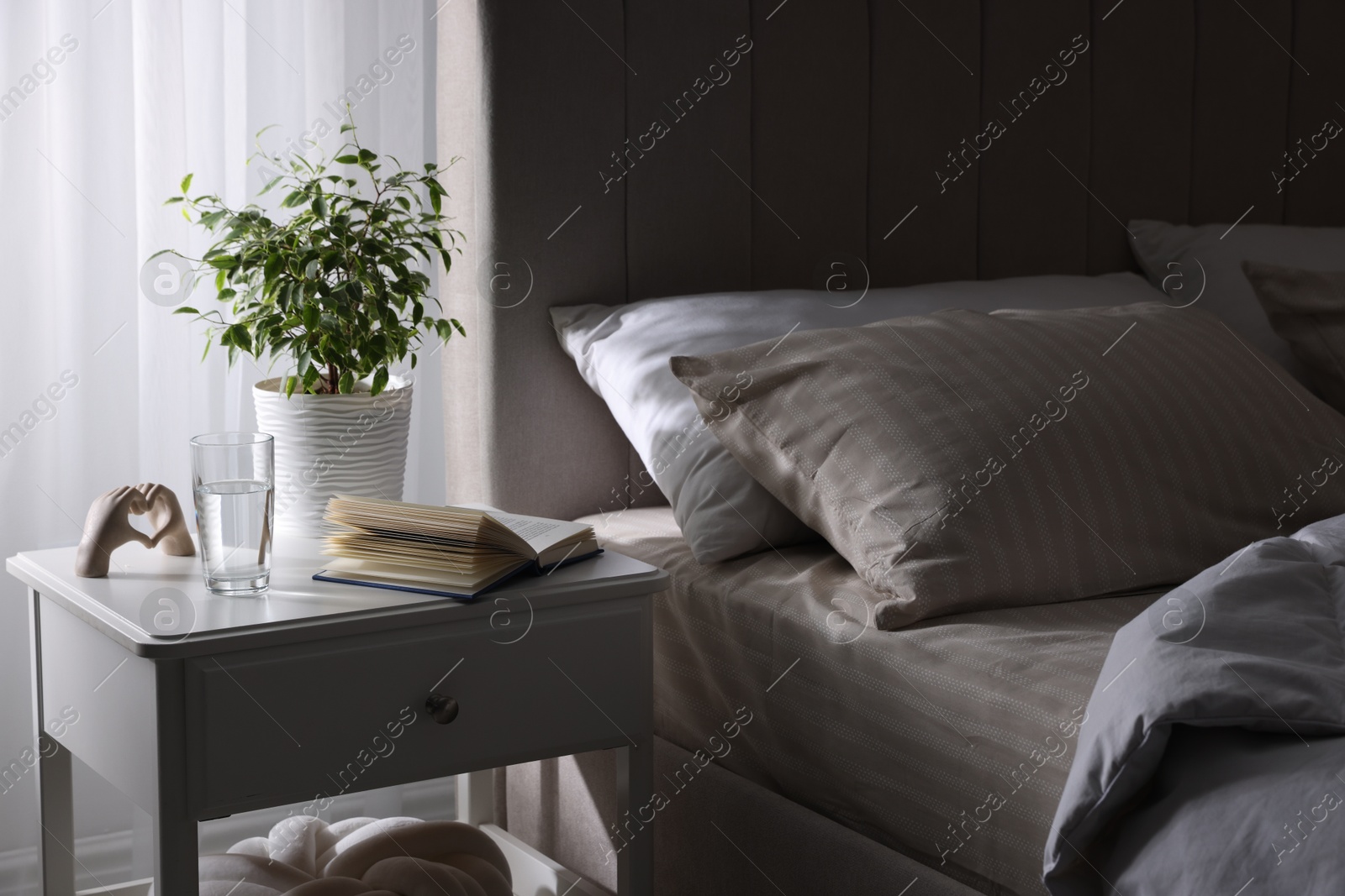 Bedside table with book, decor and glass of water near bed in room Photo of Bedside table with book, decor and glass of water near bed in room