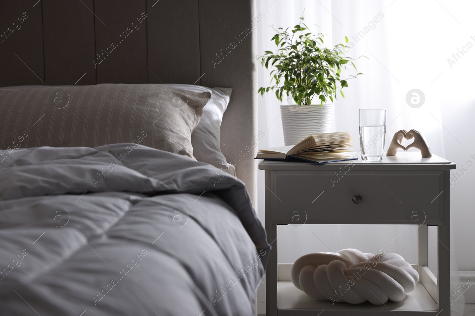 Bedside table with book, decor and glass of water near bed in room Photo of Bedside table with book, decor and glass of water near bed in room