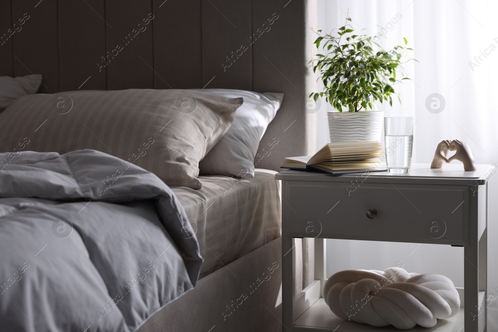 Bedside table with book, decor and glass of water near bed in room Photo of Bedside table with book, decor and glass of water near bed in room